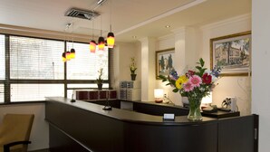 A reception desk with a vase of flowers, a lamp, and a framed picture on the wall. - Little House in Rehavia (Jerusalem)