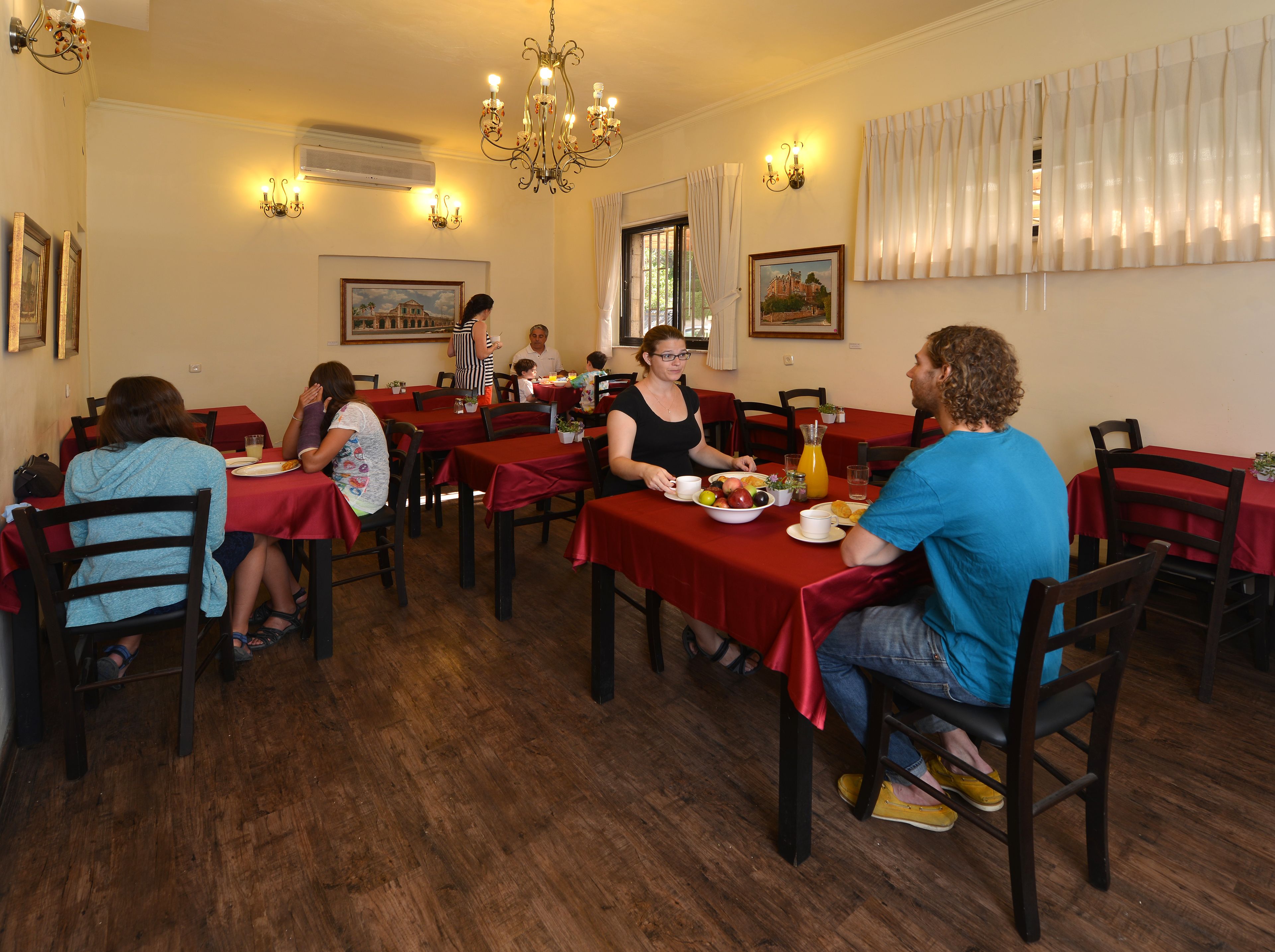 Un comedor con piso de madera, manteles rojos y un candelabro.