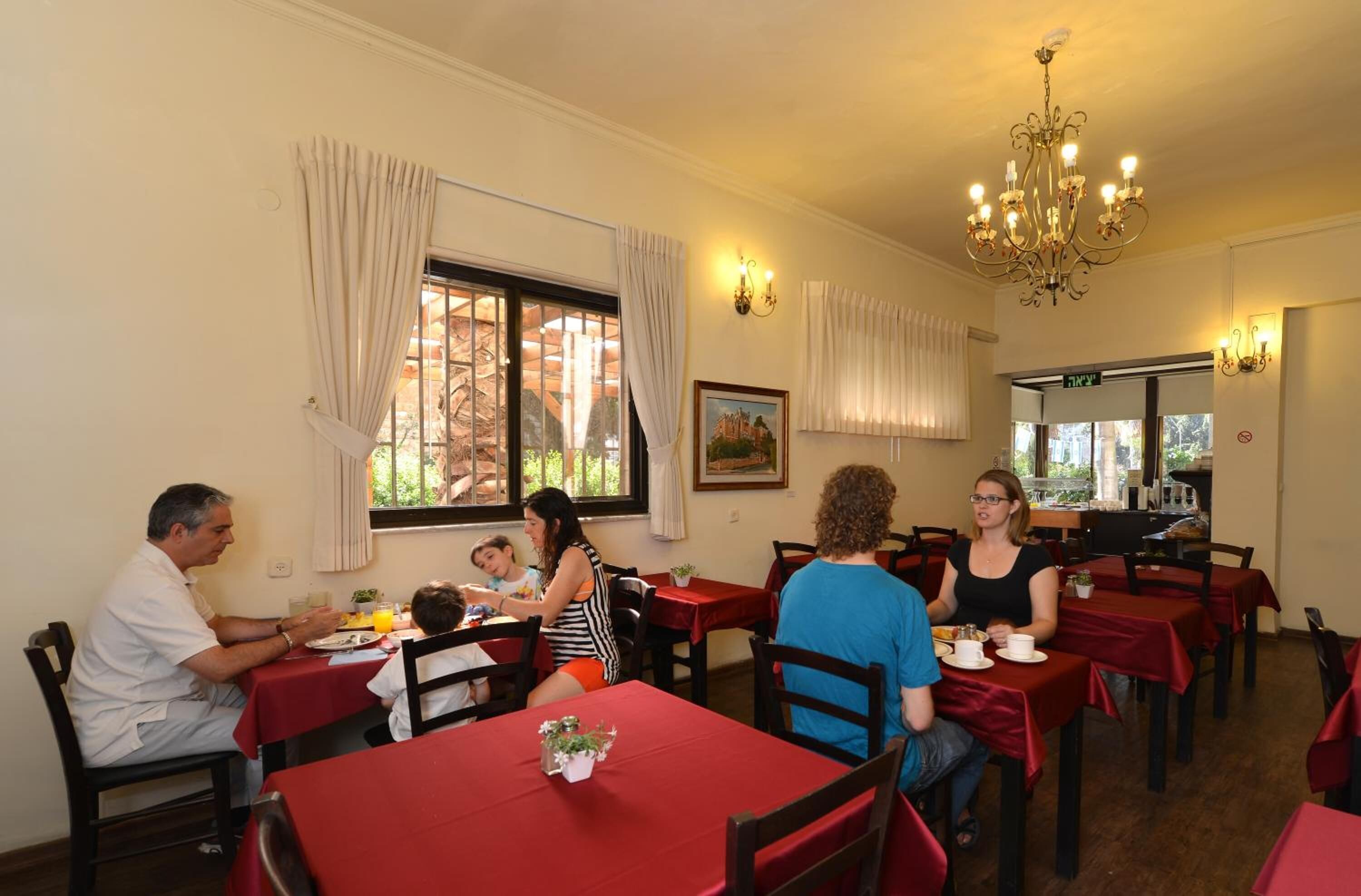 Un restaurante con mesas y sillas, un candelabro y una ventana con cortinas.