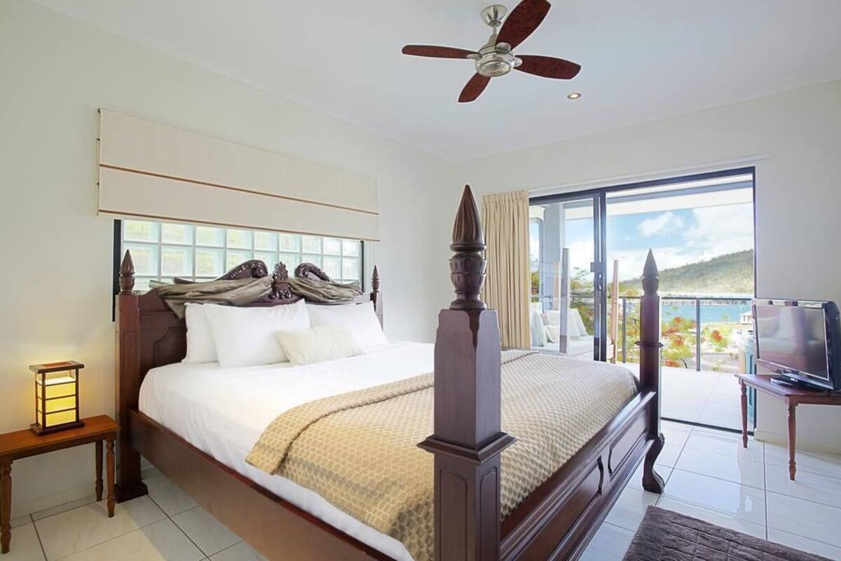 Une chambre avec un grand lit, un ventilateur de plafond, une télévision et un balcon avec vue.