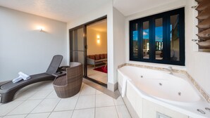 Une salle de bain moderne dotée d’une grande baignoire, d’une chaise longue et d’une porte-fenêtre coulissante donnant sur un balcon.