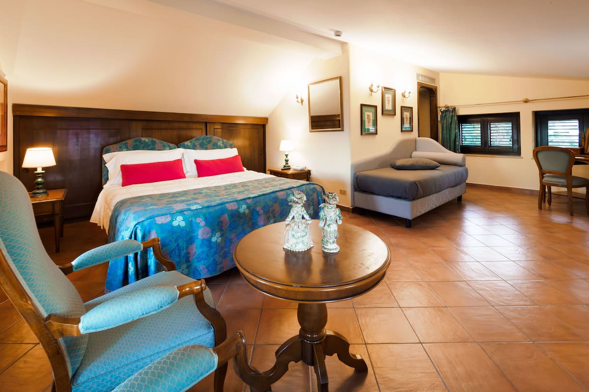 A hotel room with a bed, a sofa, a chair, a table, and a window.