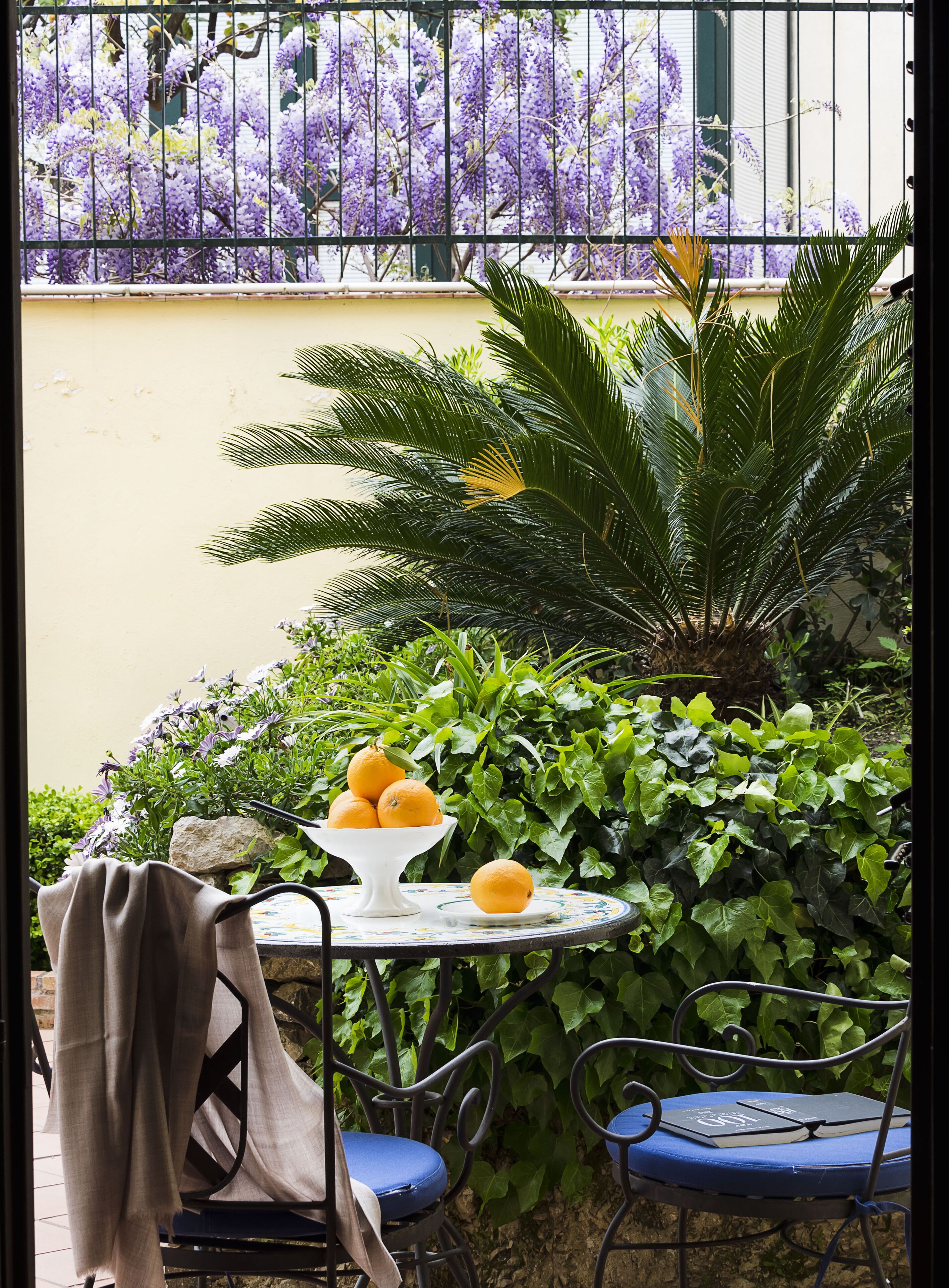 Un'area salotto all'aperto con tavolo, sedie e uno sfondo di fiori viola e verde vegetazione.