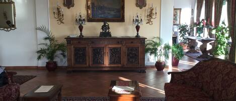 A traditional living room with a wooden cabinet, two potted plants, a red sofa, and a patterned rug.