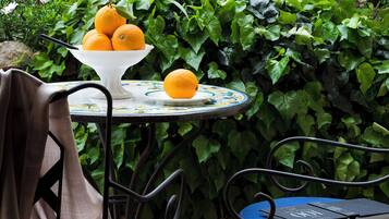 A table with a bowl of oranges, a chair, and a book.