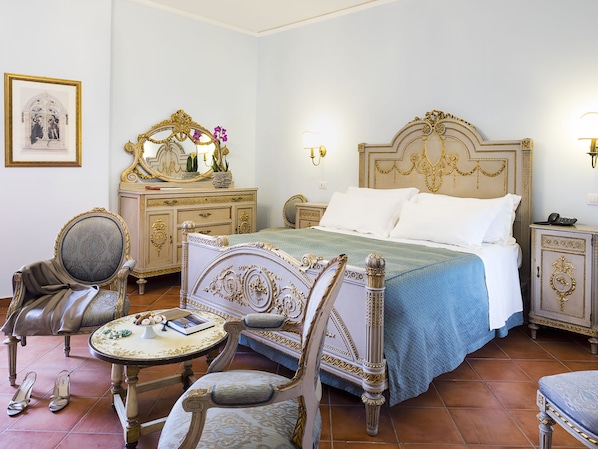 Une chambre à coucher classique et élégante, avec un grand lit, une coiffeuse avec un miroir et une petite table ronde sur laquelle sont posés un livre et une paire de chaussons.