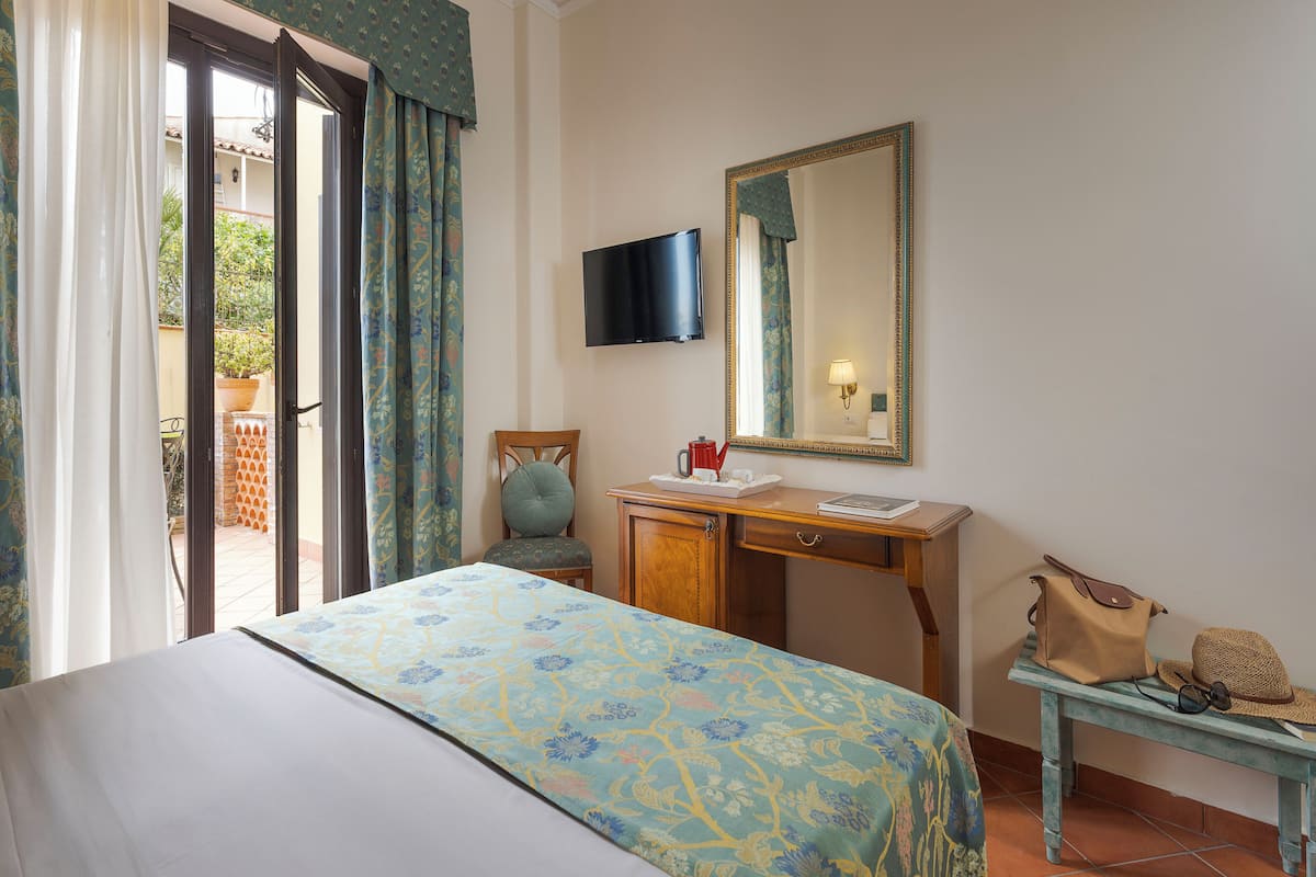 A hotel room with a bed, a desk, a television, a mirror, and a view of the outside.