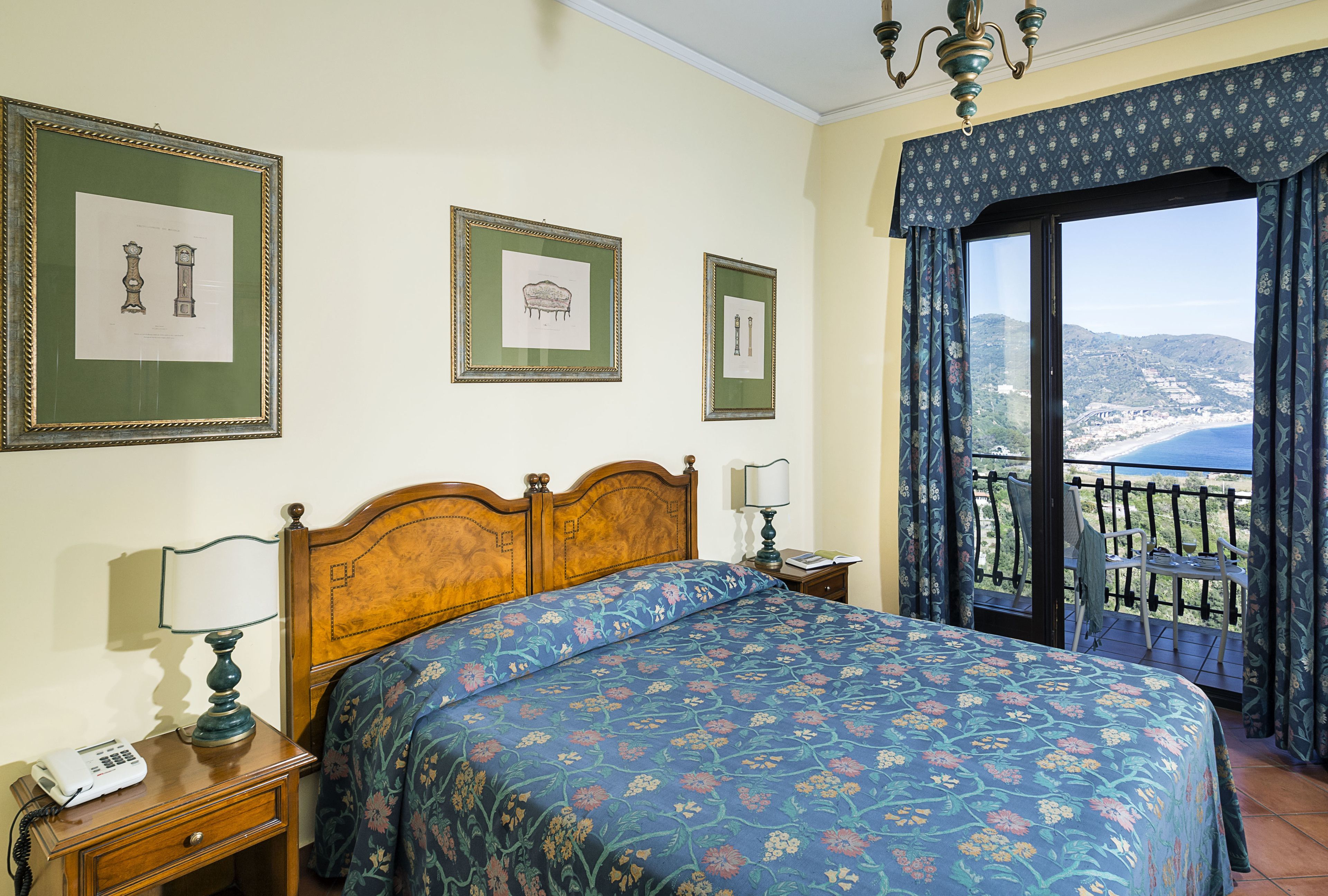 A bedroom with a bed, a nightstand with a lamp, a telephone, and framed pictures on the wall.