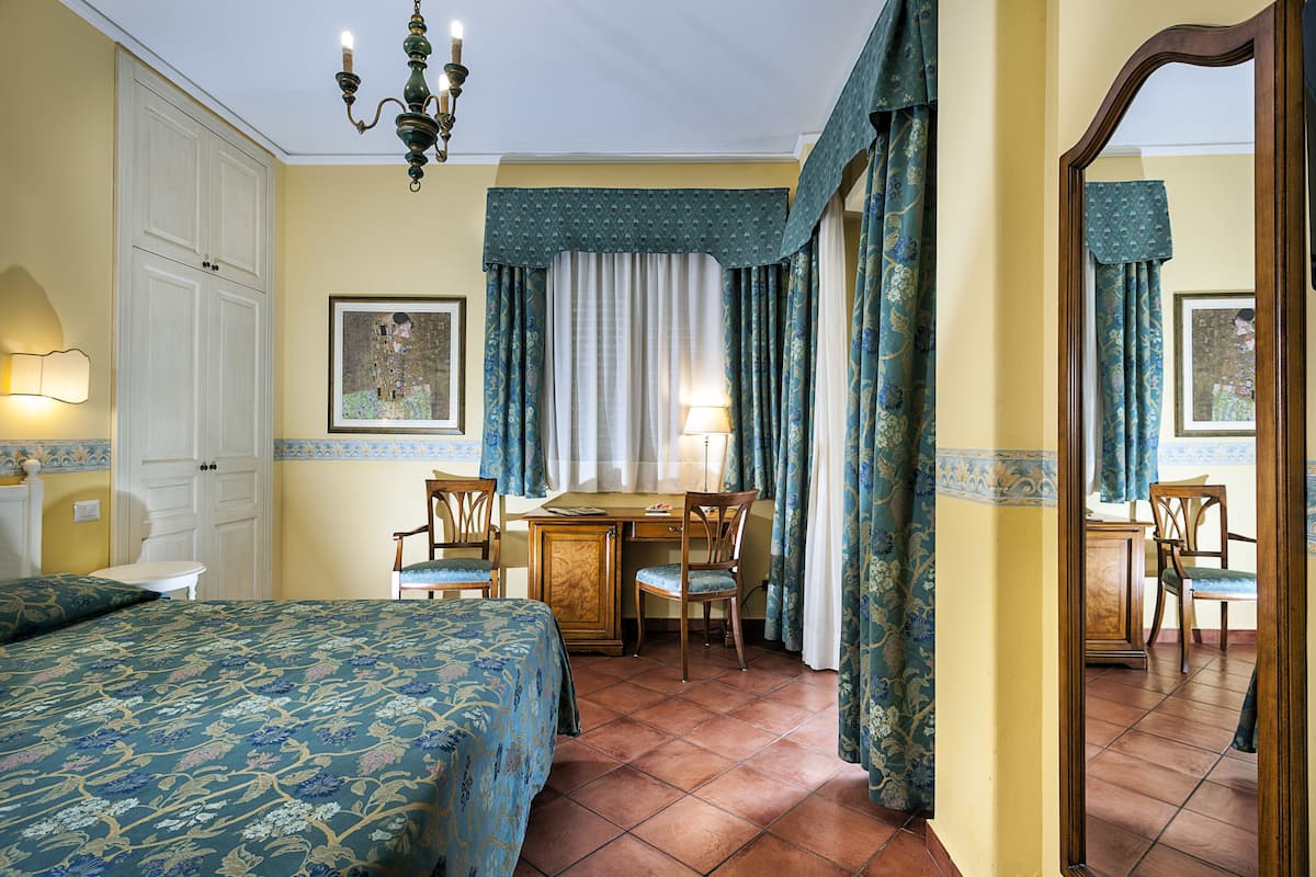 A hotel room with a bed, desk, chairs, and a mirror.