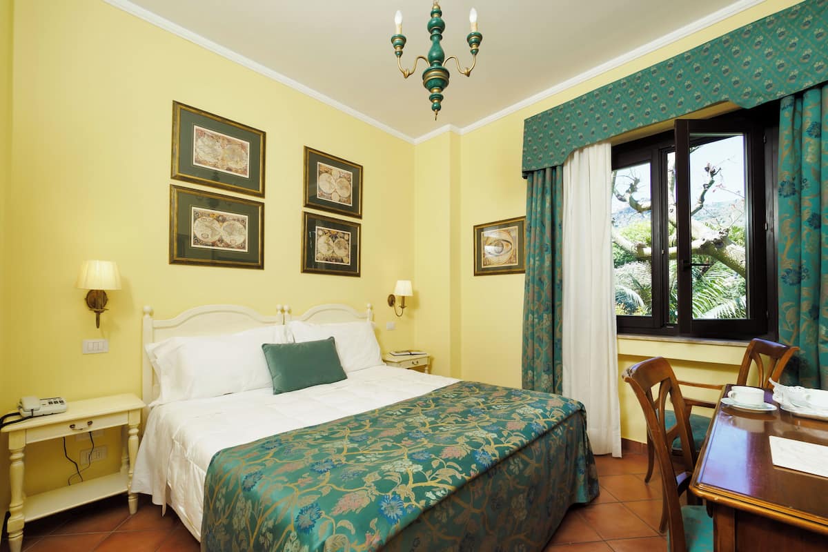 A hotel room with a bed, bedside tables, a desk, and a window with curtains.