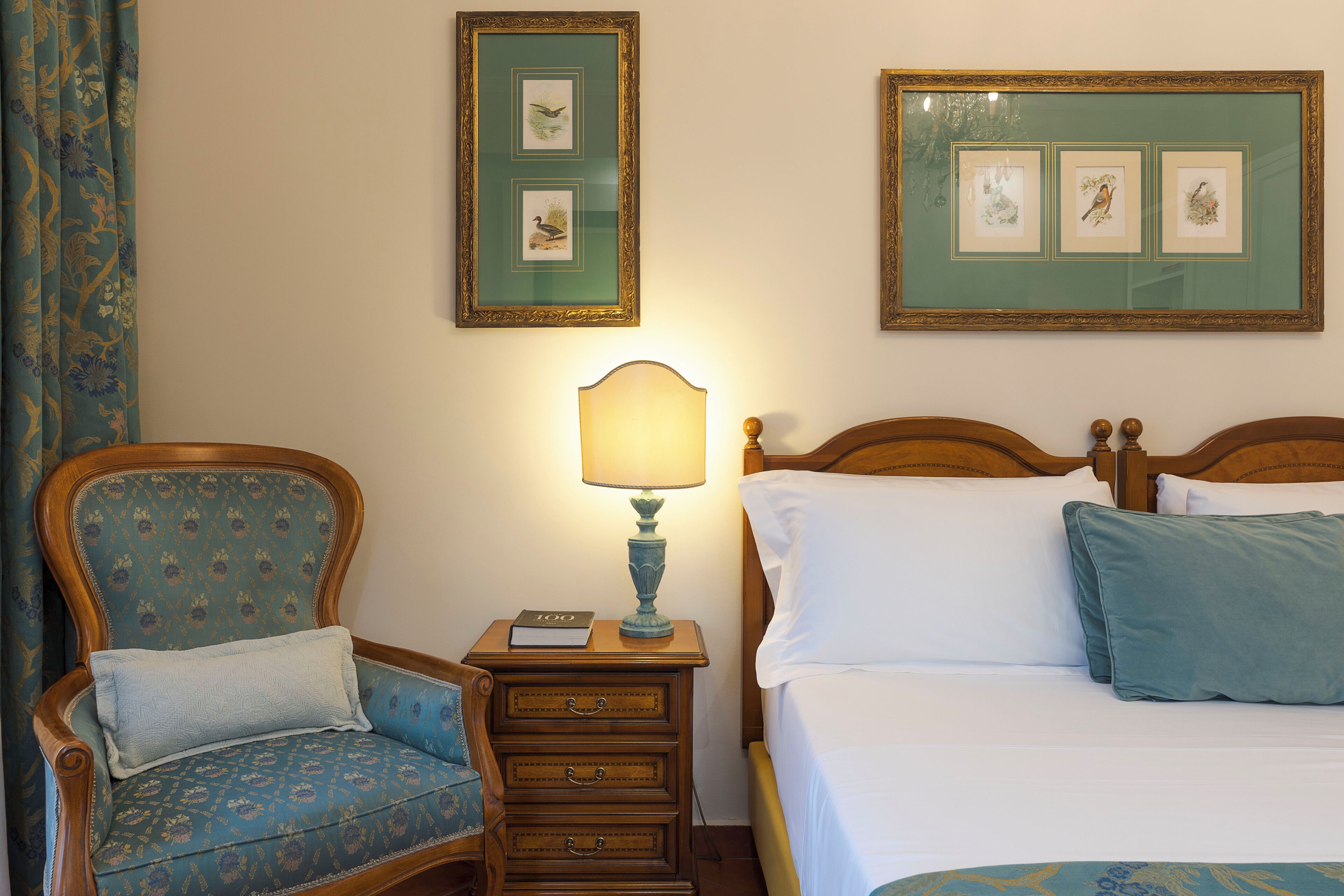 Une chambre à coucher avec un lit, une table de chevet avec une lampe, une chaise et deux tableaux encadrés au mur.