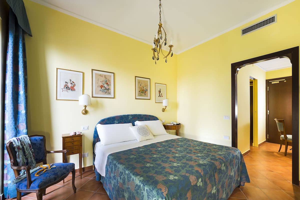 A hotel room with a bed, a chair, a desk, and a door.