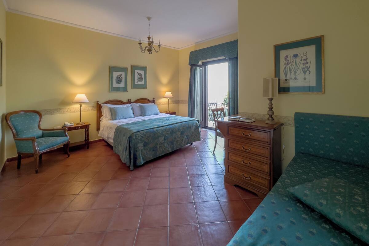 A hotel room with a bed, a chair, a desk, and a balcony.