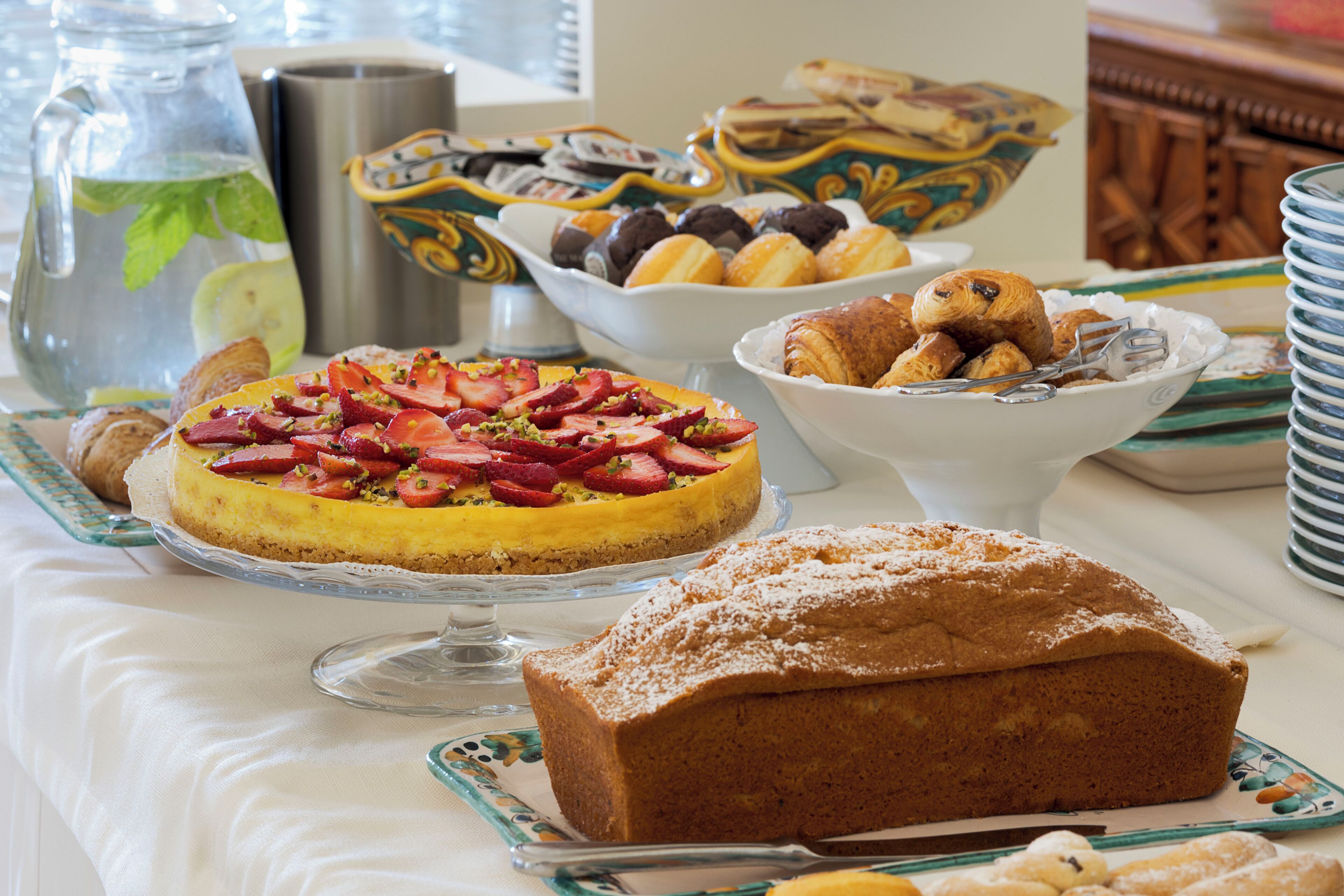 A breakfast buffet with various pastries, a fruit tart, and a loaf of bread.