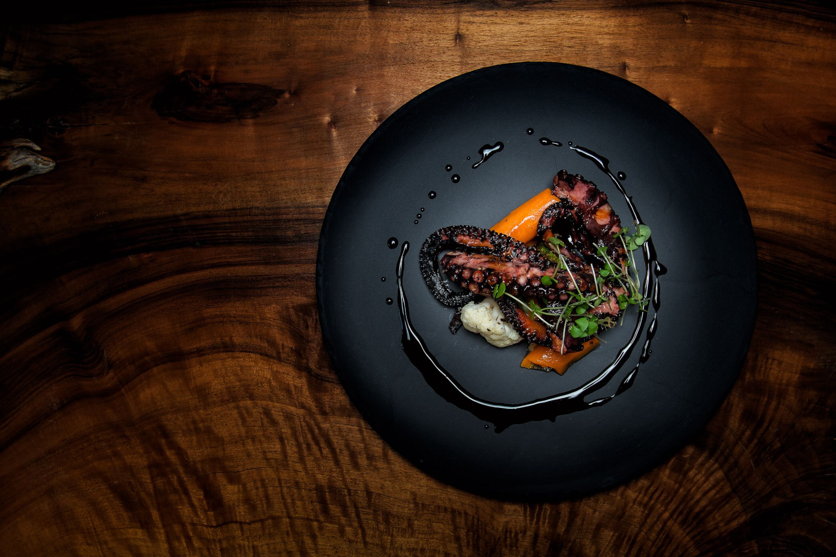 A black plate with a dish of food on a wooden table.