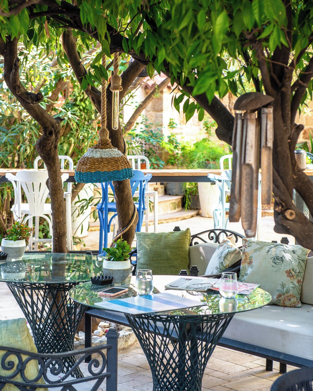 An outdoor seating area with round tables and chairs, surrounded by trees and plants.