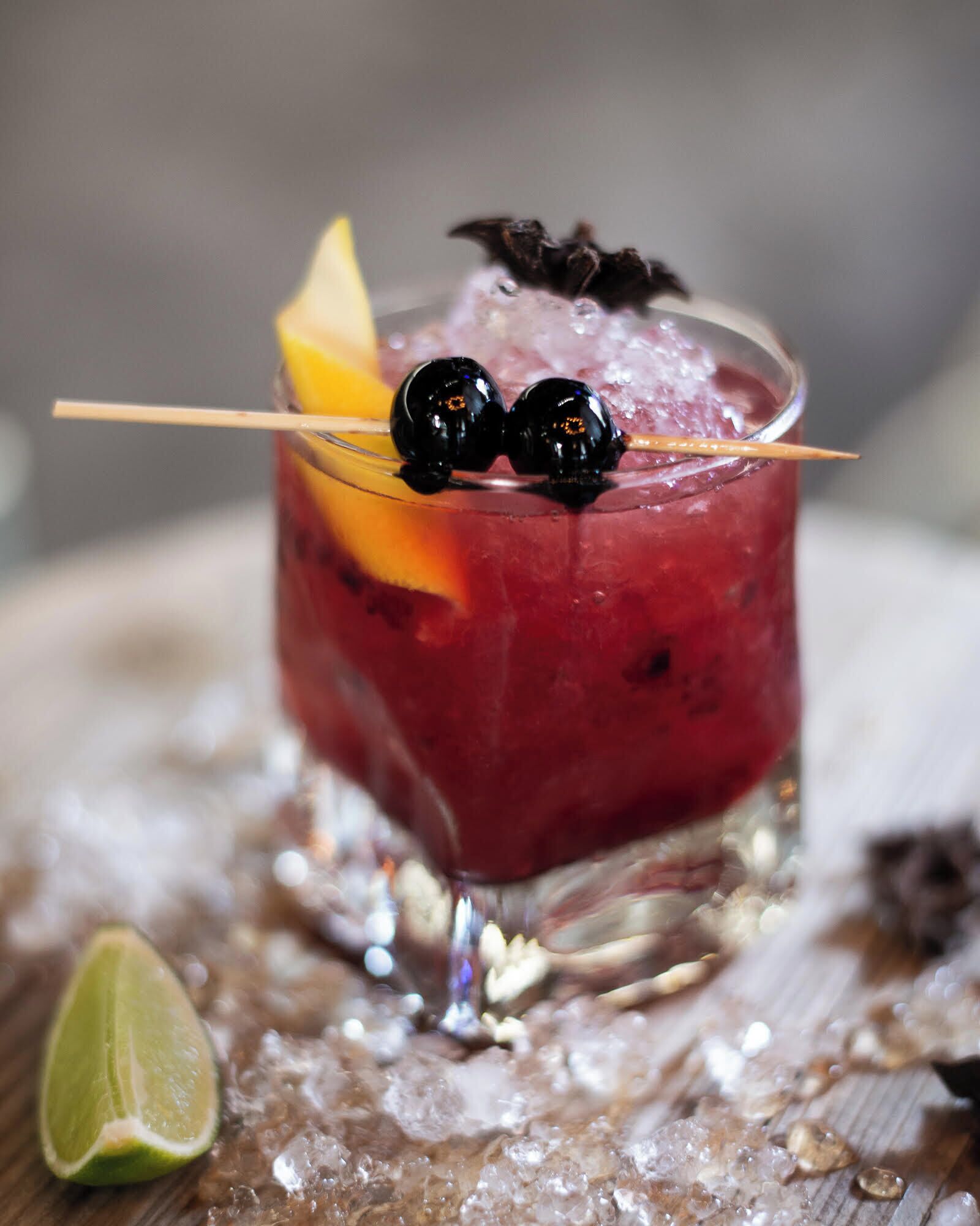 A cocktail with a lime wedge and a decorative fruit on a glass with a straw.