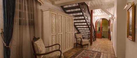 A hallway with a patterned rug, a chair, a wardrobe, and a staircase.