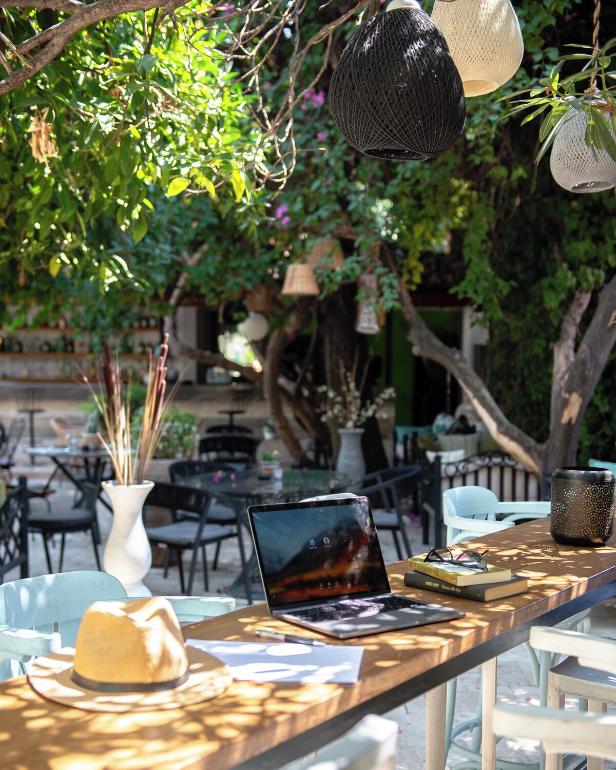 An outdoor seating area with a laptop, books, and a hat on a table.