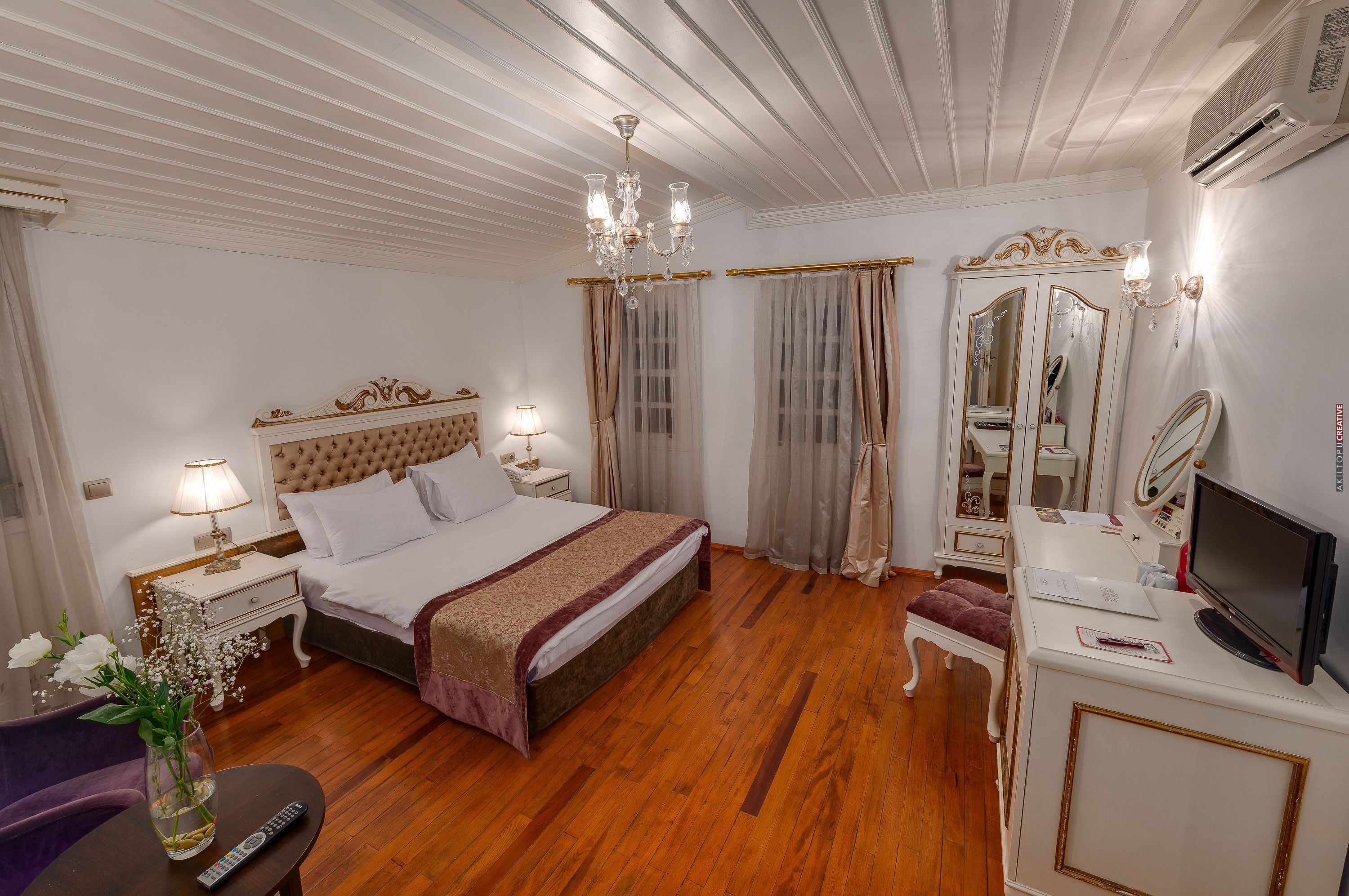 A well-appointed hotel room with a large bed, a vanity with a mirror, a television, and a desk with a lamp.
