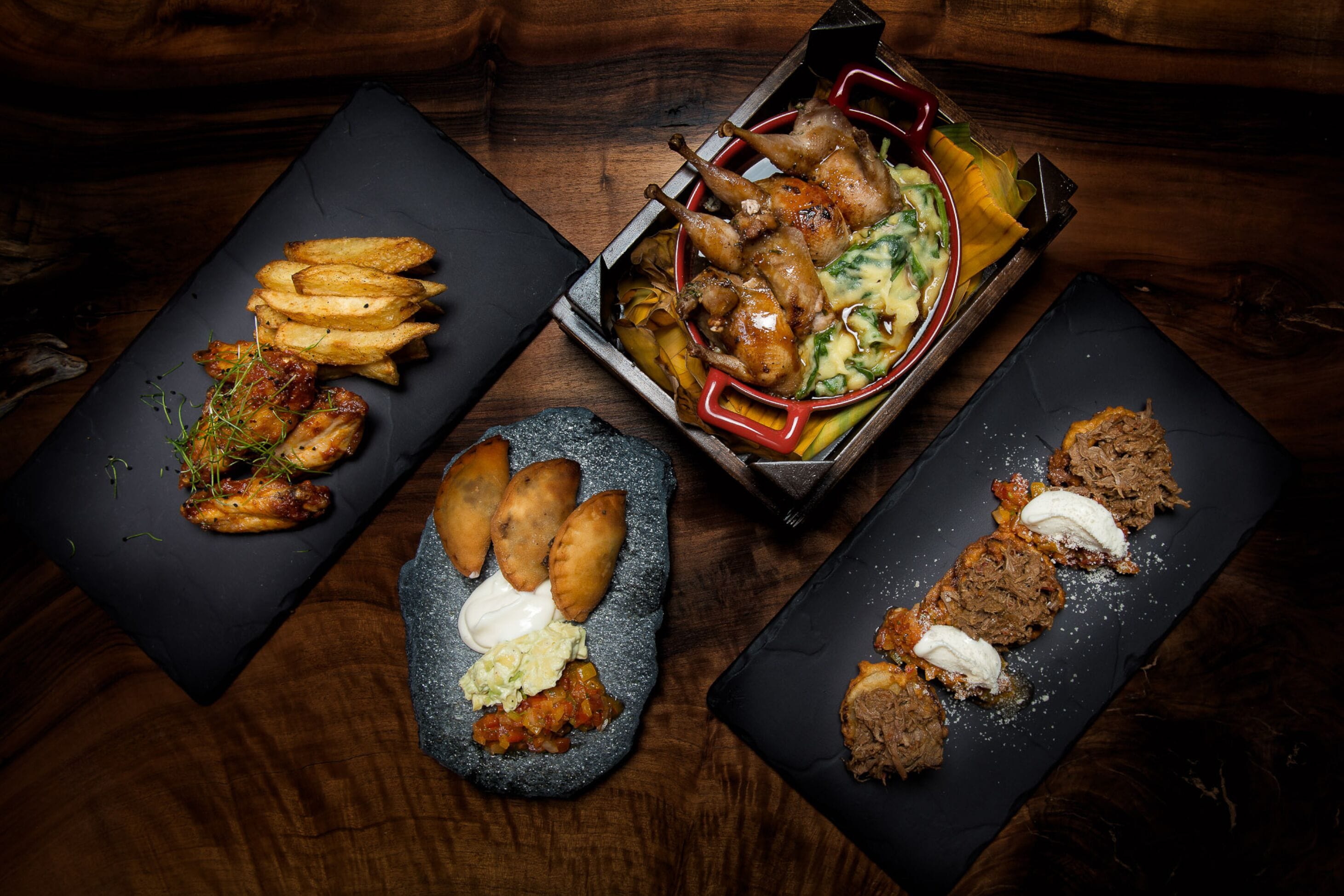 A variety of dishes including fried potatoes, meat, and pastries on slate serving boards.
