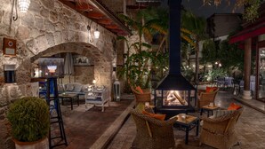 An outdoor patio area with stone walls, wicker furniture, and a central fire feature. - Tuvana Hotel - Special Class (Antalya)