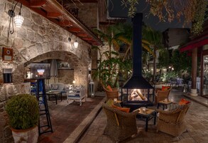 Un espace extérieur aménagé en terrasse, avec des murs en pierre, des meubles en osier et un foyer central.