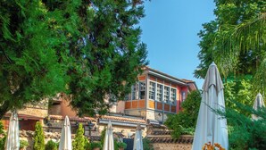 A pool area with lounge chairs and umbrellas, surrounded by trees and a building with a stone facade. - Tuvana Hotel - Special Class (Antalya)