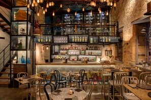 Zona de bar con diversas opciones de asientos, como mesas redondas y taburetes, además de una variedad de botellas y copas en estanterías.