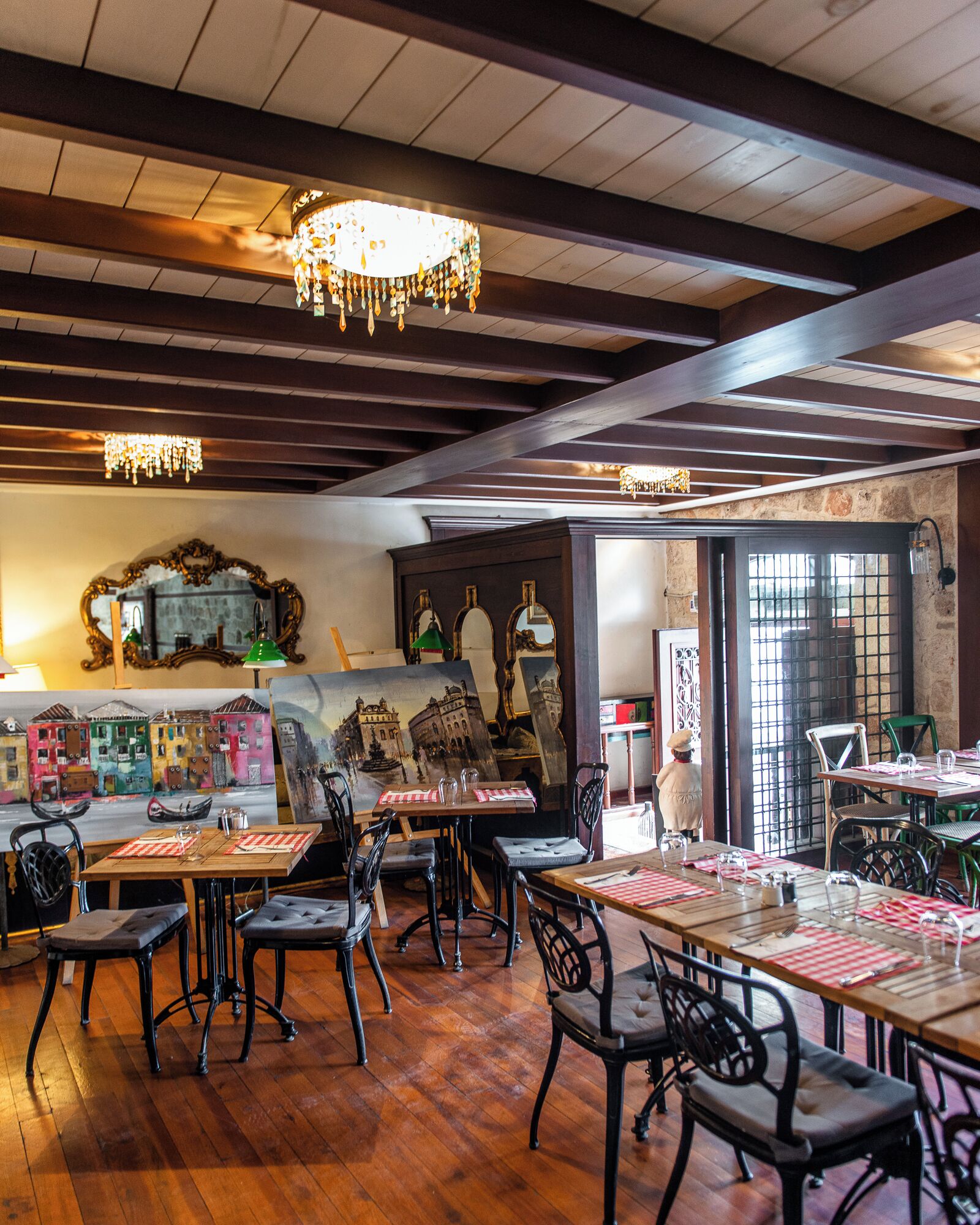A restaurant interior with wooden floors, black metal chairs, and tables set with red and white checkered tablecloths.