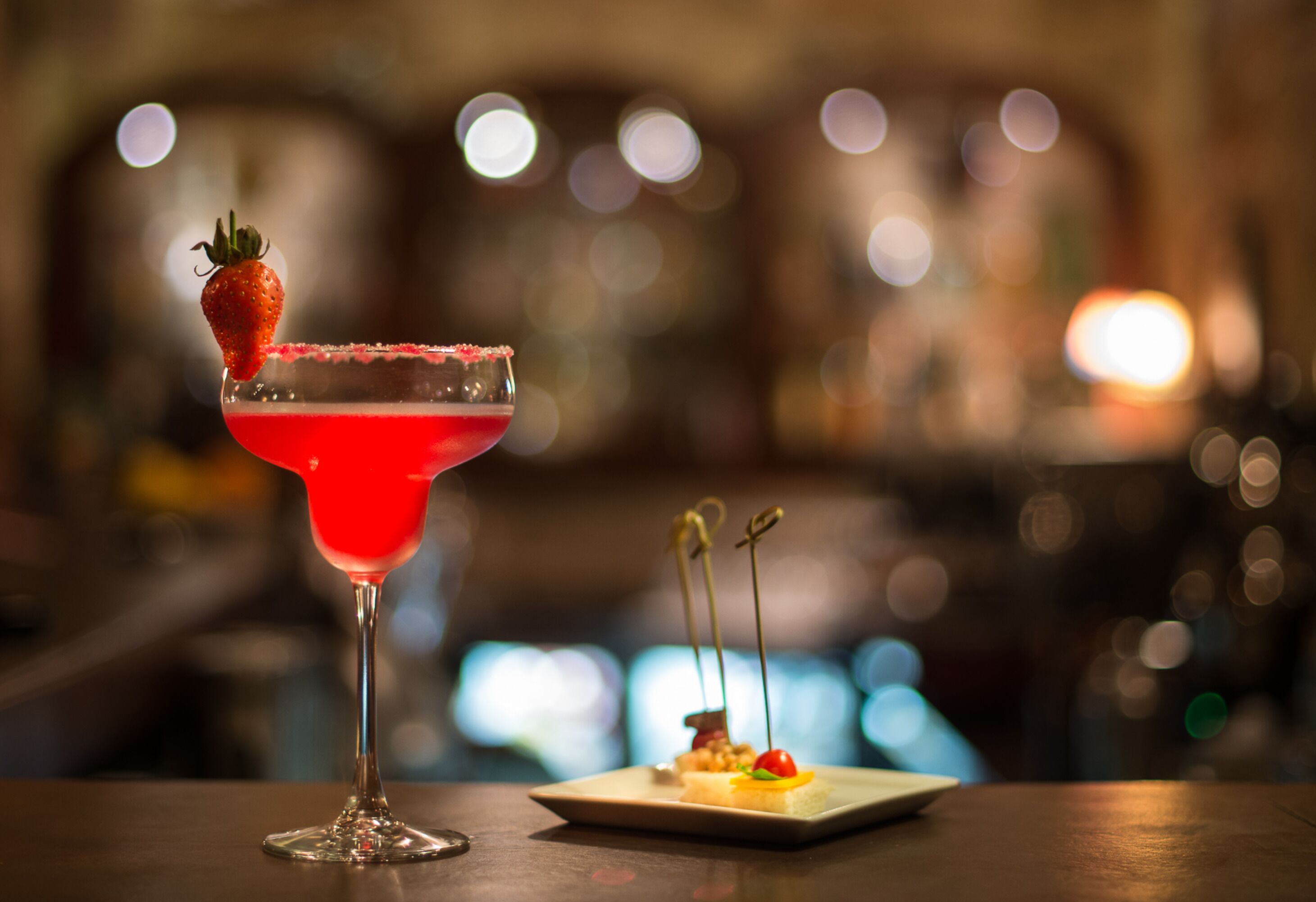 A cocktail glass with a strawberry garnish and a square plate with a dessert.