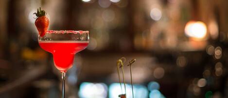 A cocktail glass with a strawberry garnish and a square plate with a dessert.