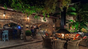 An outdoor patio area with stone arches, wicker furniture, and a central fire feature.