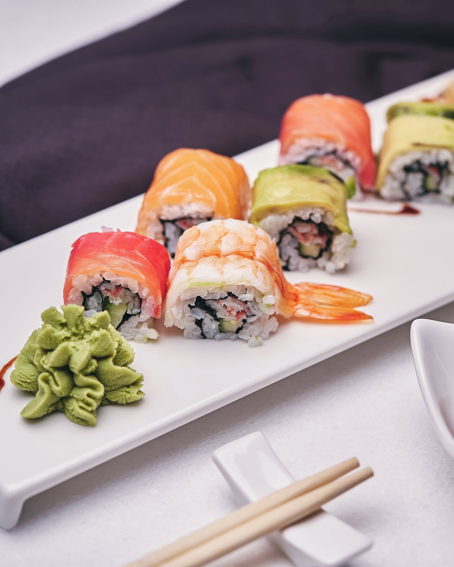 Un plato rectangular blanco con varios rollos de sushi y una pequeña porción de wasabi verde.
