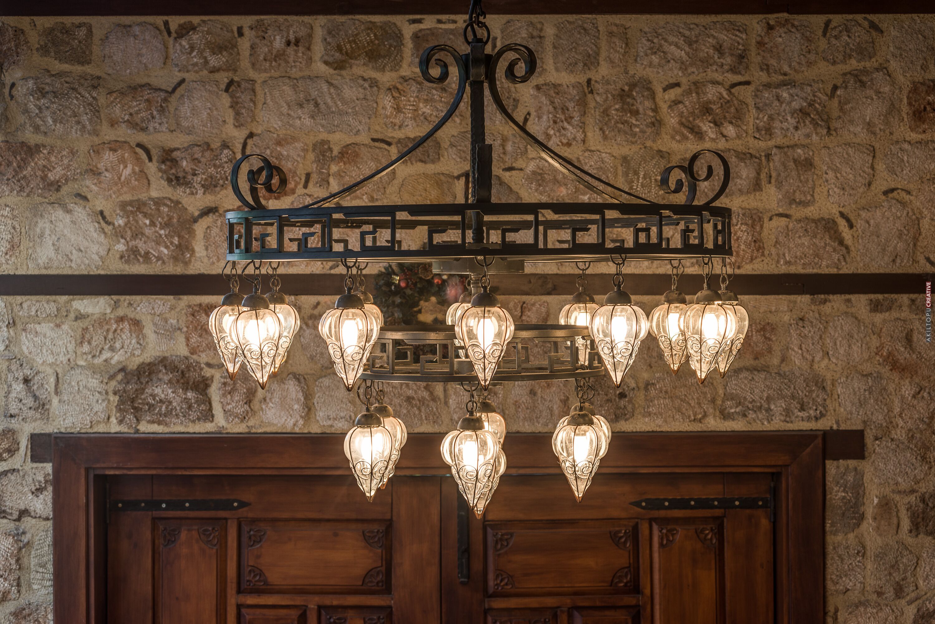 A chandelier with multiple light fixtures hanging from a metal frame against a stone wall.