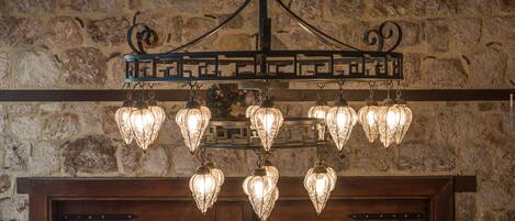 A chandelier with multiple light fixtures hanging from a metal frame against a stone wall.