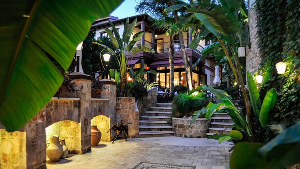 A multi-level building with a stone facade, a staircase leading to the upper levels, and a well-lit entrance area with potted plants and a decorative rug. - Tuvana Hotel - Special Class (Antalya)