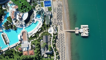 An aerial view of a resort with multiple swimming pools, a beach, and a dock.
