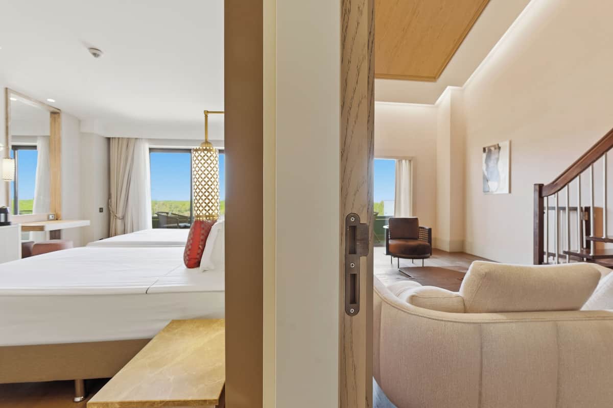 Ein modernes Hotelzimmer mit einem großen Bett, einem Holztisch, einer Couch und Blick ins Freie.