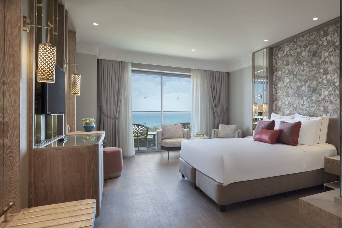 Ein modernes Hotelzimmer mit einem großen Bett, einem vom Rest getrennten Badezimmer, einer Sitzecke mit Meerblick und einem Balkon.