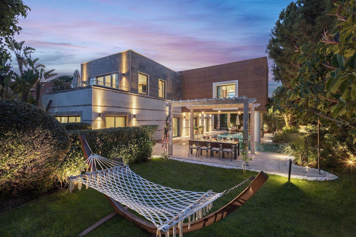 Ein modernes Haus mit Terrasse, einer Hängematte und einem Poolbereich.
