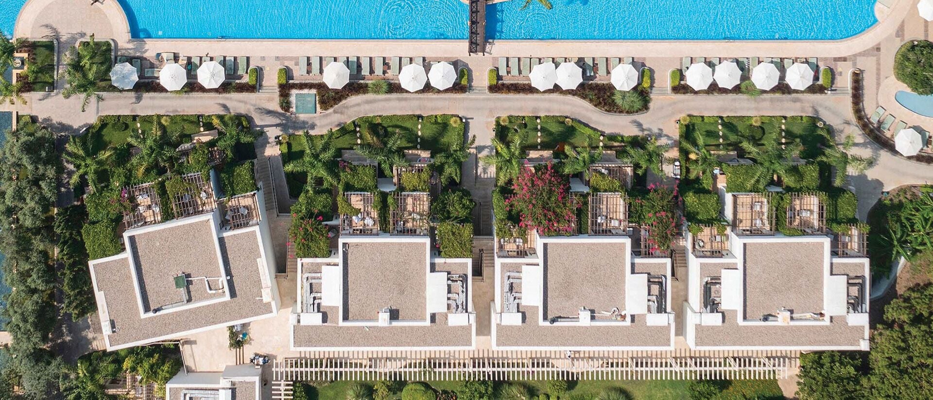 Eine Vogelperspektive zeigt ein Resort mit einem zentralen Schwimmbecken, mehreren Gästezimmern und üppiger Bepflanzung.