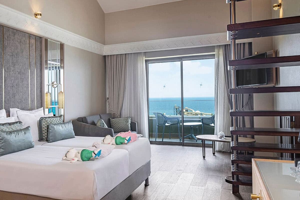 Ein Hotelzimmer mit Bett, Nachttischen, einem Spiegel und einem Balkon mit Meerblick.