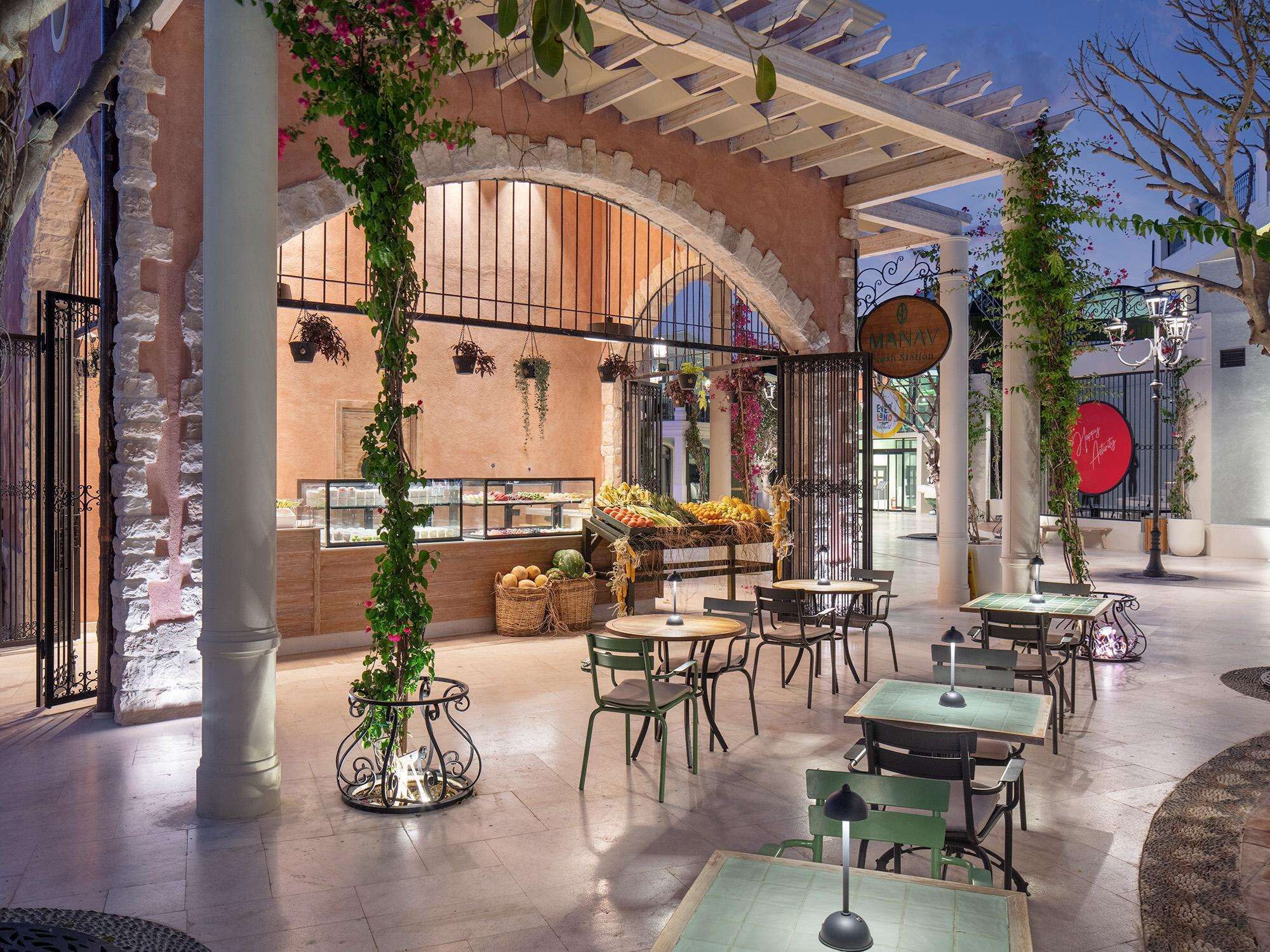 An outdoor café with tables and chairs, a fruit display, and a pergola structure.