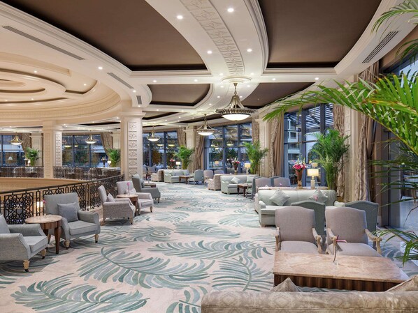 Un hall d’entrée spacieux, doté d’un tapis à motifs, de plusieurs espaces aménagés pour s’asseoir et de grandes fenêtres offrant une vue dégagée.