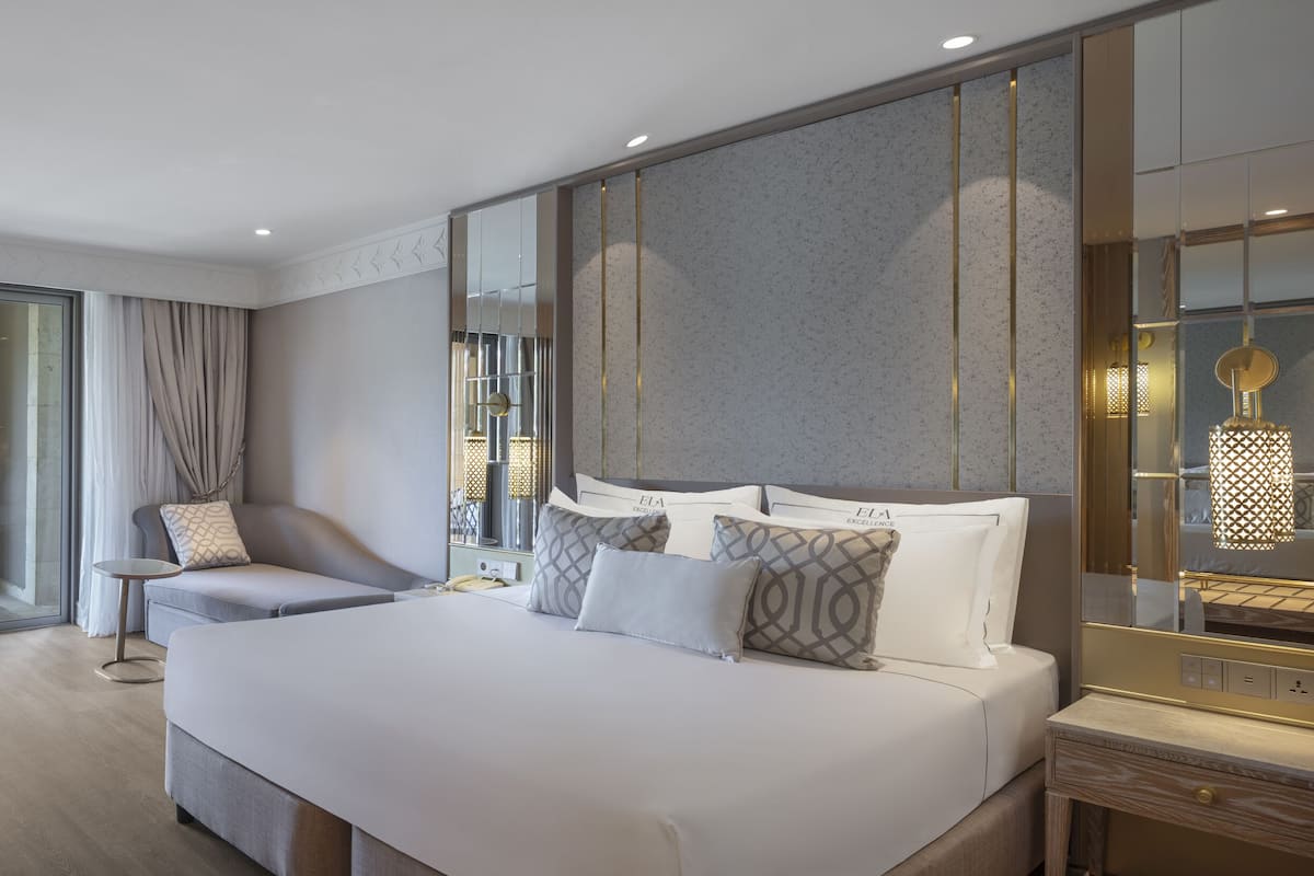 Ein modernes Hotelzimmer mit einem großen Bett, einer Sitzecke mit kleinem Tisch und einem Balkon mit Vorhängen.