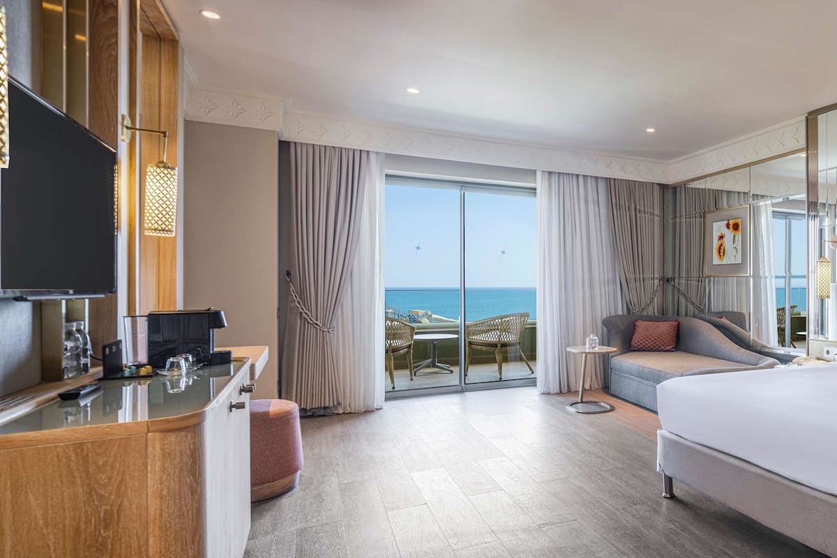 Ein Hotelzimmer mit einem großen Bett, einer Sitzecke, einem Schreibtisch und Blick aufs Meer.
