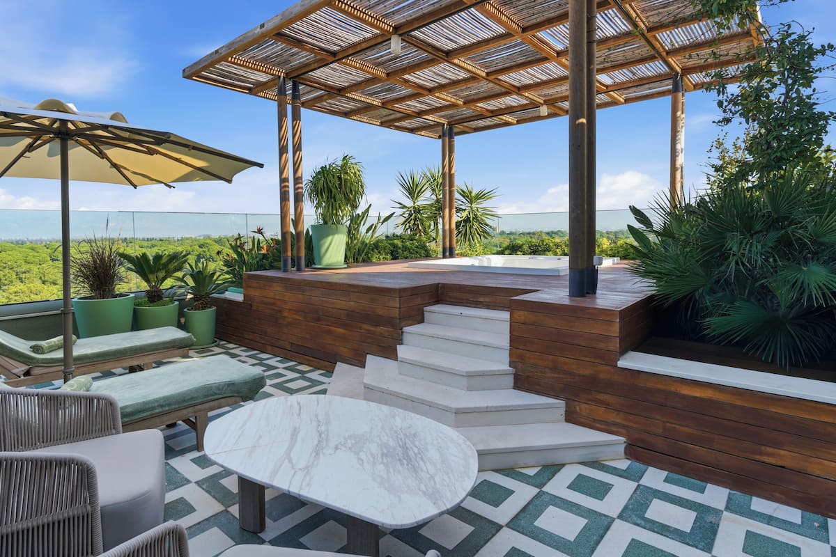 Eine Terrasse im Freien mit einer Holz-Pergola, einem Marmortisch, gepolsterten Sitzmöbeln und Blick auf die Landschaft.