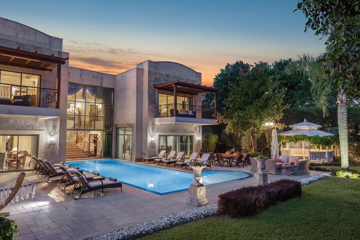 Ein modernes, zweistöckiges Haus mit Swimmingpool, Sitzgelegenheiten im Freien und üppiger Bepflanzung.