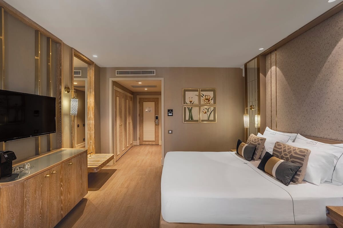 Ein Hotelzimmer mit einem großen Bett, einem Fernseher auf einer Holzkassette und einem Flur, der zu anderen Zimmern führt.